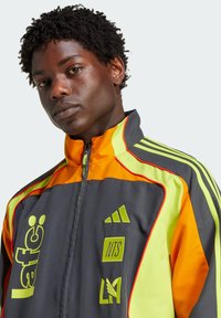 Grijze en oranje sportjack met neonaccenten, voorzien van een ritssluiting, logo's en gestreepte ontwerpdetails langs de schouders.