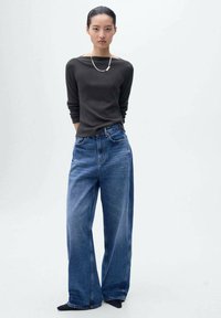 Tricou lung cu mânecă întunecată și blugi largi de culoare bleu. Tricoul are un decolteu tip barcă și o textură moale. Blugii au un design clasic cu cinci buzunare.