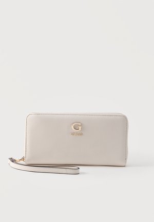 Porte-monnaie bracelet en cuir texturé beige Guess avec logo doré "G" et fermeture éclair, posé sur une surface blanche.