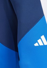 Marineblauwe en helderblauwe sportbroek met een gladde textuur, schuine kleurvlakken en witte logoaccenten.