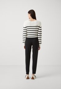 Hvit og svart stripete strikket genser med cropped design, kombinert med svarte smale bukser og joggesko.