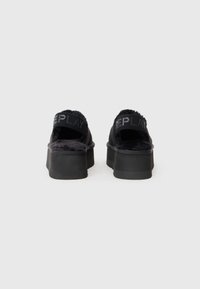 Pantofi slip-on negri cu platformă, căptușiți cu blană sintetică și textul "REPLAY" pe curelele de la toc, prezentați din spate pe un fundal alb.