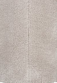 Pehmeä, vaaleanbeige sherpa-fleece-kangas, tiheä ja kiharainen rakenne, ja näkyvä sauma kulkee pystysuunnassa keskellä.