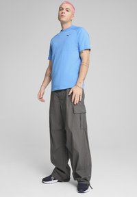 Tricou scurt de culoare albastru deschis, cu un logo mic, purtat împreună cu pantaloni cargo gri închis, care au buzunare laterale și o croială relaxată.