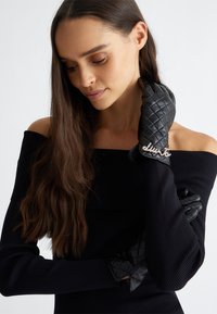 Guanti in pelle nera con un design trapuntato e un dettaglio in argento. I guanti hanno una vestibilità aderente e elegante, che mette in risalto una texture liscia.