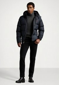 Granatowa pikowana kurtka z kapturem, zamkiem błyskawicznym i logo; pod spodem szary golf; czarne dopasowane spodnie; czarne botki za kostkę.