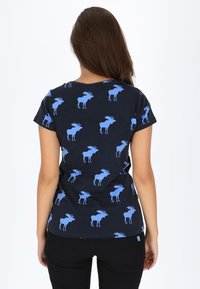 Blauwe elandpatroon op een marineblauwe t-shirt met korte mouwen, met een ronde halslijn en een getailleerde snit. Zwarte broek zichtbaar aan de onderkant.