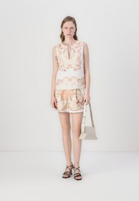 Top sin mangas con estampado floral en blanco y durazno, combinado con shorts a juego. Presenta un borde de encaje y un bolso sencillo. Sandalias con tiras entrelazadas.