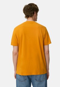 Kortærmet t-shirt med rund hals i lys orange bomuld. Har en afslappet pasform og ensfarvet ryg, kombineret med blå denim jeans.