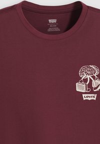 Mørkerød bomulds T-shirt med et grafisk design af en hjerne og en aktetasker. Afslappet pasform og rund halsudskæring. Levi's logo nederst.