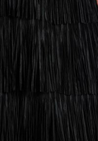 Textil negro con flecos verticales en capas y textura suave. Cada capa está espaciada de manera uniforme, creando un patrón rítmico.