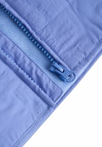 Tessuto azzurro chiaro con una texture liscia presenta una cerniera nascosta, un tirazip coordinato e un morbido rivestimento interno di una tonalità simile.
