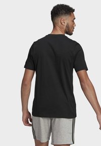 Musta puuvillapaita lyhyillä hihoilla, pyöreällä kaula-aukolla ja rentona istuvuudella, yhdistettynä harmaisiin shortseihin, joissa on mustat sivuraidat.