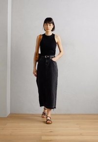 Musta tank-top, joka on yhdistetty tumman farkkuiseen midi-hameeseen. Asusteessa on vyötäröllä vyö ja kaupungille sopivat nauhakengät, minimalistista taustaa vasten.