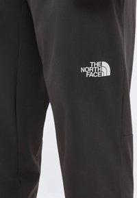 Μαύρο παντελόνι The North Face με λευκό λογότυπο τυπωμένο στο άνω μέρος του μηρού, εμφανιζόμενο σε κοντινό πλάνο στο δεξί πόδι.