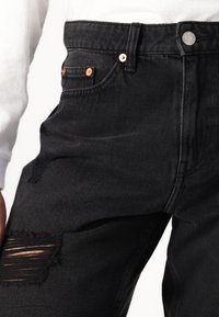 Sorte denim jeans med slidte knædetaljer, kobberhardware og høj talje. Har traditionelle lommer og en lige ben design.