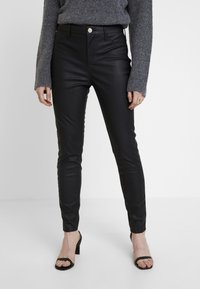 Černé skinny kalhoty z umělé kůže s vysokým pasem, předními kapsami a lesklým povrchem, doplněné černými sandály na středním podpatku.