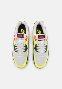 Nike-sneakers med en ljus färgdesign i vitt, svart och neonaccenter. Tillverkade av syntetiska material, snörning och vadderad krage.