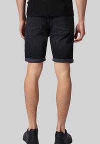 Czarne dżinsowe szorty o luźnym kroju, z podwiniętymi nogawkami, dwoma tylnymi kieszeniami i gładką teksturą, w zestawie z czarnymi trampkami.