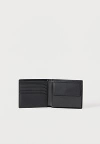 Ανοικτό δίπτυχο πορτοφόλι από μαύρο δέρμα, με τέσσερις θήκες για κάρτες στα αριστερά και θήκη για κέρματα με καπάκι στα δεξιά, σε απλό λευκό φόντο.