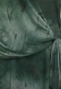 Tissu tie-dye vert avec un nœud froncé sur le côté droit, montrant des plis doux et des variations subtiles de texture.