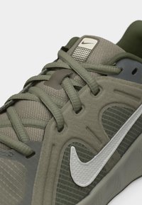 Κοντινή λήψη πράσινου αθλητικού παπουτσιού Nike που δείχνει υφασμάτινη υφή, κορδόνια, επενδυμένο σχέδιο και λευκό λογότυπο Nike Swoosh στην πλευρική επιφάνεια.