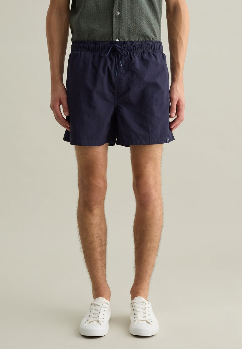Costumi da bagno blu navy realizzati in tessuto leggero, con vita elasticizzata e coulisse, e tasche laterali per comodità.