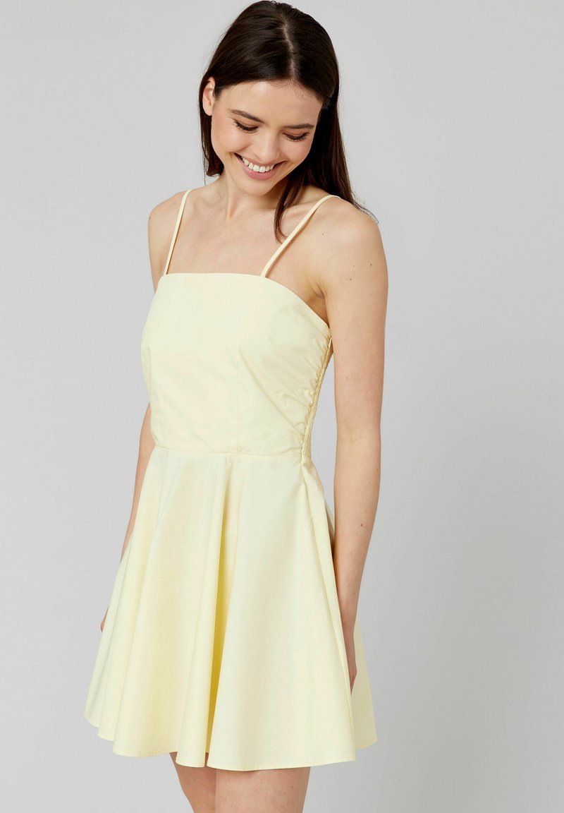 Robe A-line jaune avec bretelles spaghetti, corsage cintré et jupe évasée. Présente des panneaux latéraux texturés et une finition en tissu lisse.