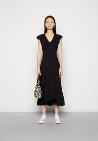 Vestido maxi preto com mangas curtas em babados, corpete ajustado e saia em camadas. Combinado com ténis brancos e uma bolsa com padrão de zebra.