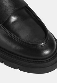 Zwarte leren schoen met een ronde neus, gladde oppervlakte, gestikte accenten en een dikke rubberen zool. Voorzien van een brede leren band over de bovenkant.