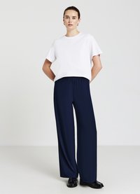 T-shirt bianca a maniche corte abbinata a pantaloni larghi blu navy con vita elastica, texture liscia e scarpe nere.