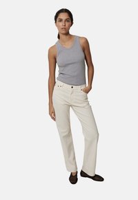 Camiseta sin mangas gris, pantalones crema con cinco bolsillos, diseño de pierna recta, textura lisa, usados con zapatos oscuros tipo slip-on.
