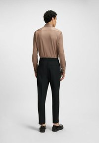 Bruine langemouwen shirt met een gladde textuur, gecombineerd met zwarte taps toelopende broek. Beide kledingstukken hebben een minimalistisch ontwerp en een elastische taille.