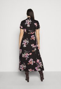 Musta kukkakuvioinen maximekko, jossa on vartalonmyötäinen vyötärö, lyhyet hihat ja kaulus. Mekossa on värikkäitä kukkakuoseja vaaleanpunaisissa, purppuran ja oranssin sävyissä.