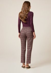 Haut à manches longues bordeaux au design ajusté, associé à un pantalon à carreaux brun taille haute. Le pantalon a une coupe ajustée et une texture lisse.