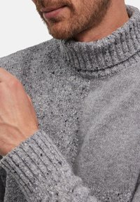 Maglione grigio a maglia con colletto alto a coste e motivo testurizzato. Il tessuto appare morbido con una vestibilità ampia e polsini a coste.