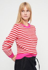 Punaste ja valgete triipudega kampsun, mis on valmistatud pehmest materjalist. Omaduseks on roosa ümara kaelusega ja äärega ning pikad, kergelt püksisäärega varrukad.