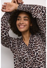 Blouse en imprimé léopard avec des manches longues et froncées. Fabriquée dans un tissu lisse, elle présente un décolleté drapé avec des motifs noirs et bruns.