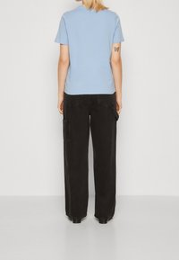 Ljusblå kortärmad t-shirt som kombineras med löst sittande svarta cargobyxor med sidofickor och en något texturerad yta.
