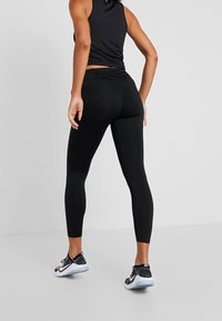 Leggings noirs avec une texture lisse et un design ajusté, comprenant une ceinture avec un accent texturé et associés à des chaussures de sport noires.