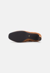 Braunes Wildleder-Schuh mit einer glatten, runden Zehenpartie und einer schwarzen Gummisohle. Enthält seitliche Verzierungen und einen niedrigen Absatz für Stabilität.