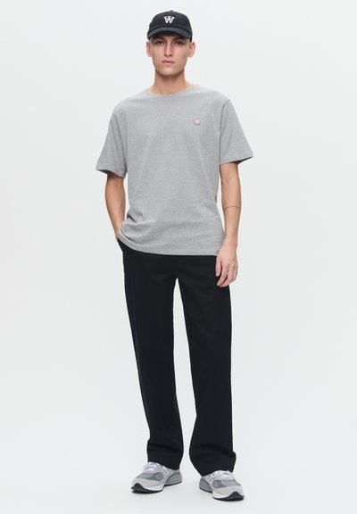 Gray cotton t-shirt with short sleeves and a small logo on the chest, paired with black trousers and gray sneakers. Black cap with a logo.