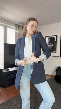 Blazer azul marinho com um corte ajustado e punho riscado, usado sobre uma t-shirt branca e jeans azuis. Tecido suave e design minimalista.