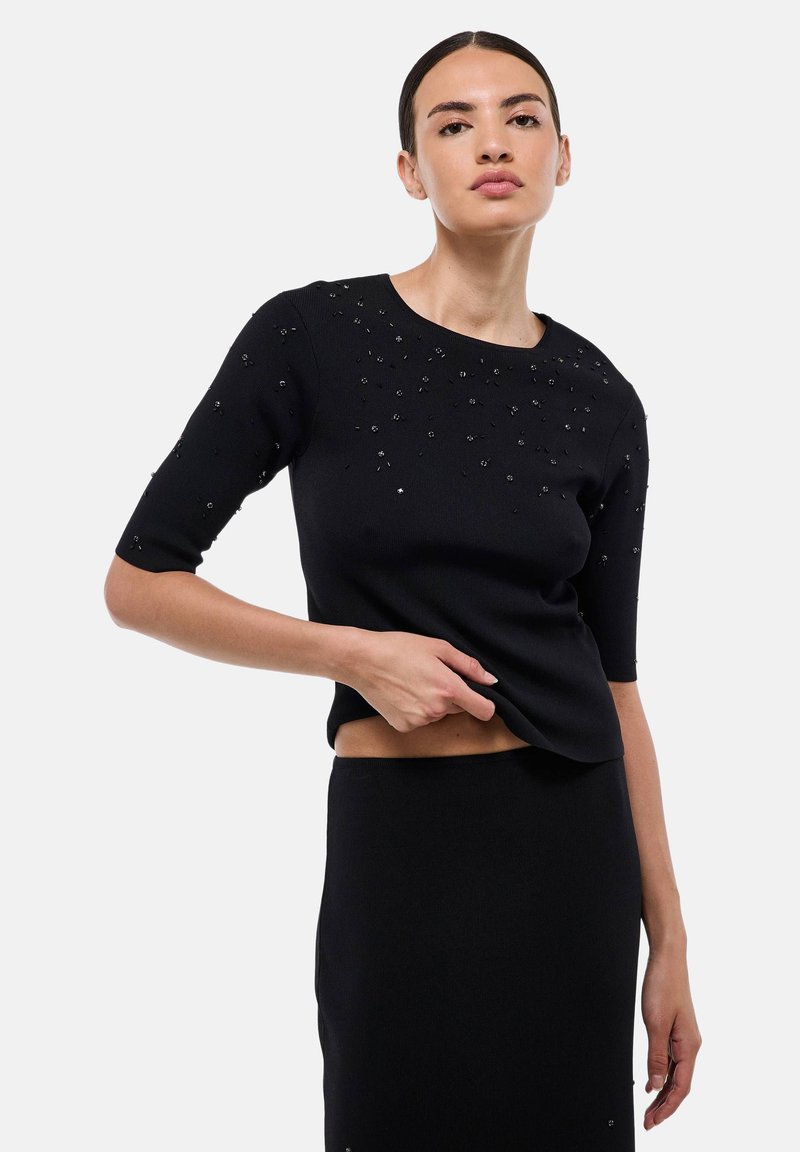 Haut noir en tricot à manches courtes avec des embellissements texturés au niveau du col. Conception ajustée avec un col rond. Accompagné d'une jupe assortie.