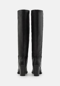 Bottes en cuir noires montantes jusqu'au genou avec un design épuré, dotées d'un talon carré et de coutures discrètes à l'arrière. Texture lisse.