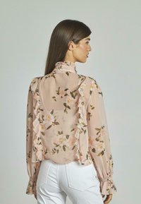 Blusa floreale color pesca con colletto e maniche arricciati, realizzata in tessuto trasparente e con un delicato motivo floreale in tonalità di rosa e verde.