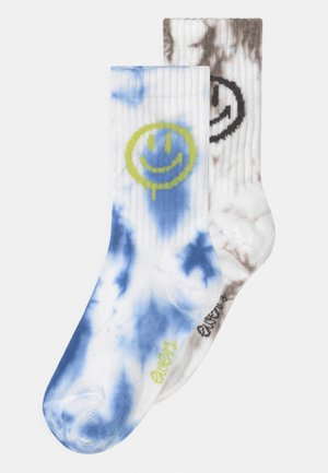 Calzini di cotone con un motivo tie-dye; un lato blu con una faccina sorridente verde e l'altro lato marrone con una faccina sorridente nera.