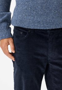 Blauw gespikkeld gebreid trui met ribgebreide manchetten, gecombineerd met donkerblauwe corduroy broek met verticale strepen en zichtbare zijzakken.