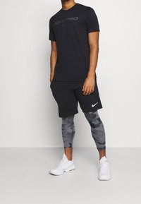 Svart Nike Pro t-shirt, svarta shorts och grå camouflage leggings som kombineras med vita sportskor. Enkelt design, fukttransporterande material.