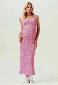 Rochie maxi de maternitate roz cu un model de frunze, design fără mâneci, detaliu cu fundă laterală și material moale, asortată cu adidași albi.